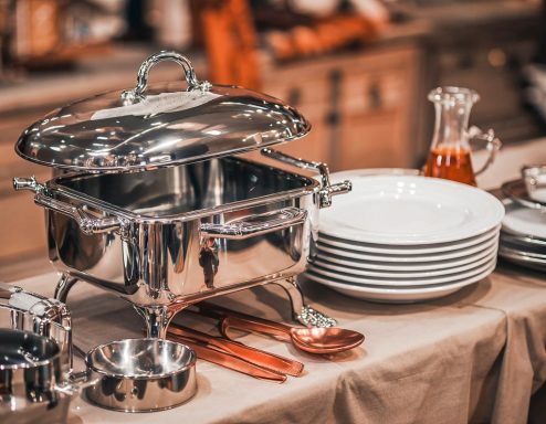 Elegantes Buffet mit silbernem Speisegeschirr und weißen Tellern auf einem Tisch.