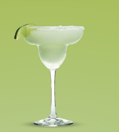 Ein Margarita-Glas mit grünem Hintergrund und einer Limettenscheibe am Rand.