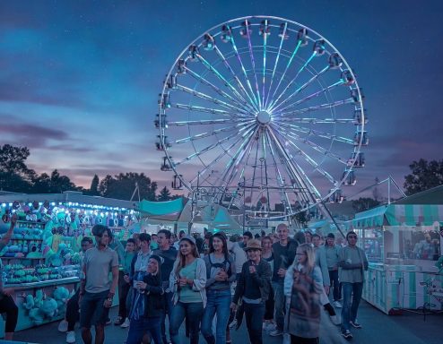Riesenrad vor einem festlichen Markt mit bunten Lichtern und Menschenmengen.