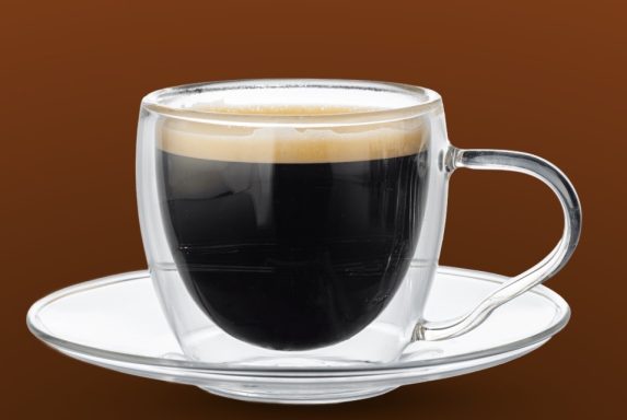 Schwarzer Kaffee in einer durchsichtigen Tasse auf einem weißen Unterteller.