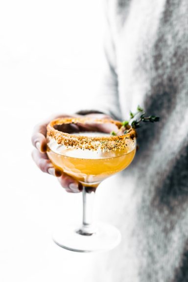Ein Glas mit orangefarbenem Cocktail, dekoriert mit einer Limettenscheibe und einem Zweig Thymian.