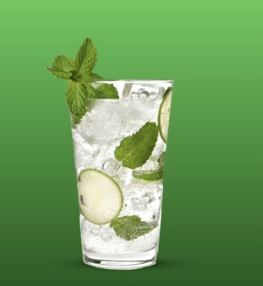 Glas mit Mojito, Eis, Limettenscheiben und frischer Minze, auf grünem Hintergrund.